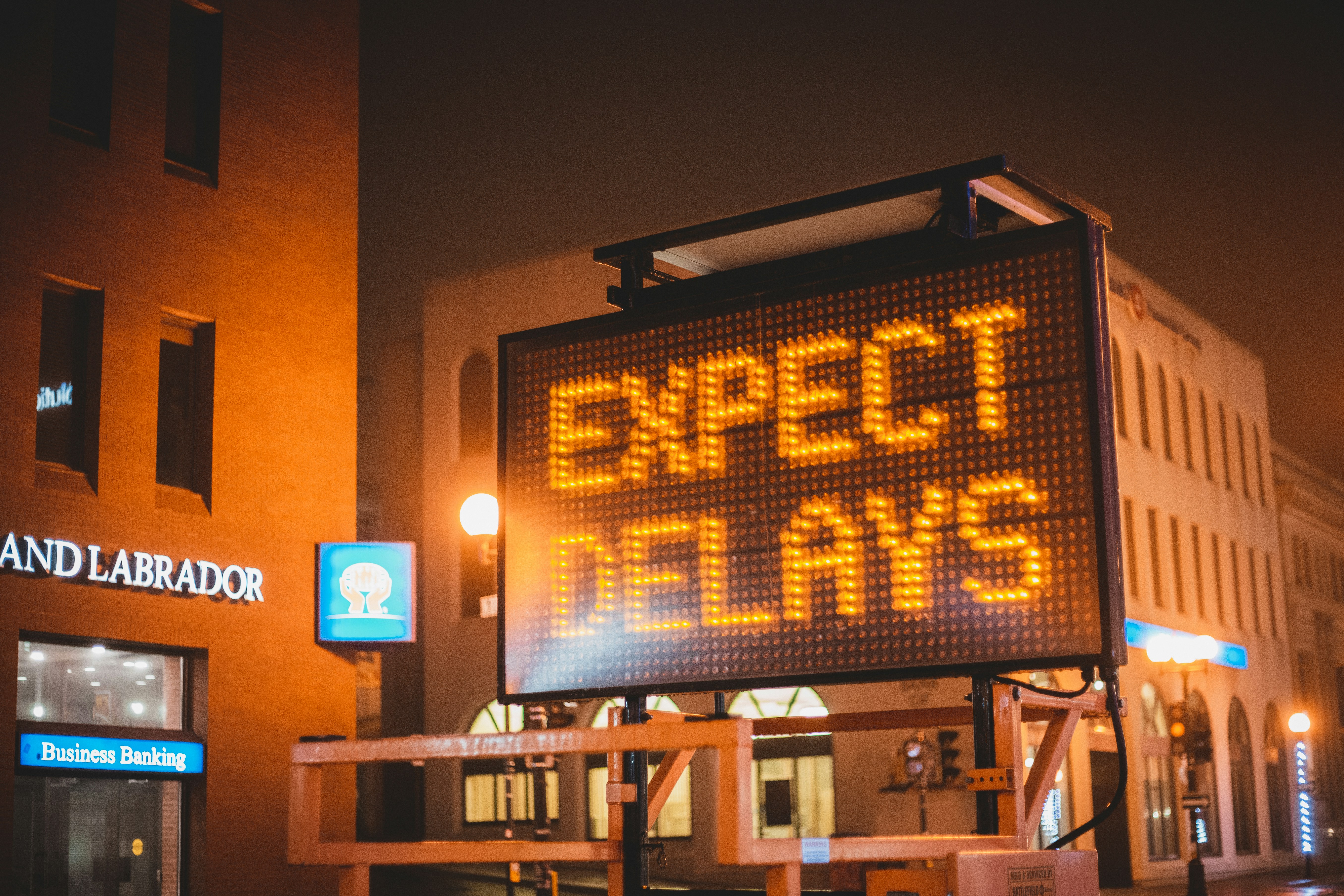 Illuminated road sign at night reading expect delays