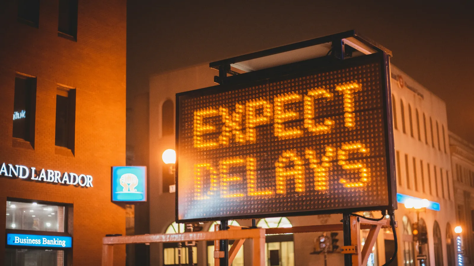 Illuminated road sign at night reading expect delays
