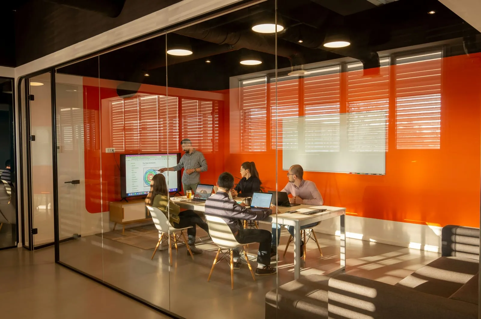 Project team meeting in a modern glass-walled conference room reviewing a schedule on screen