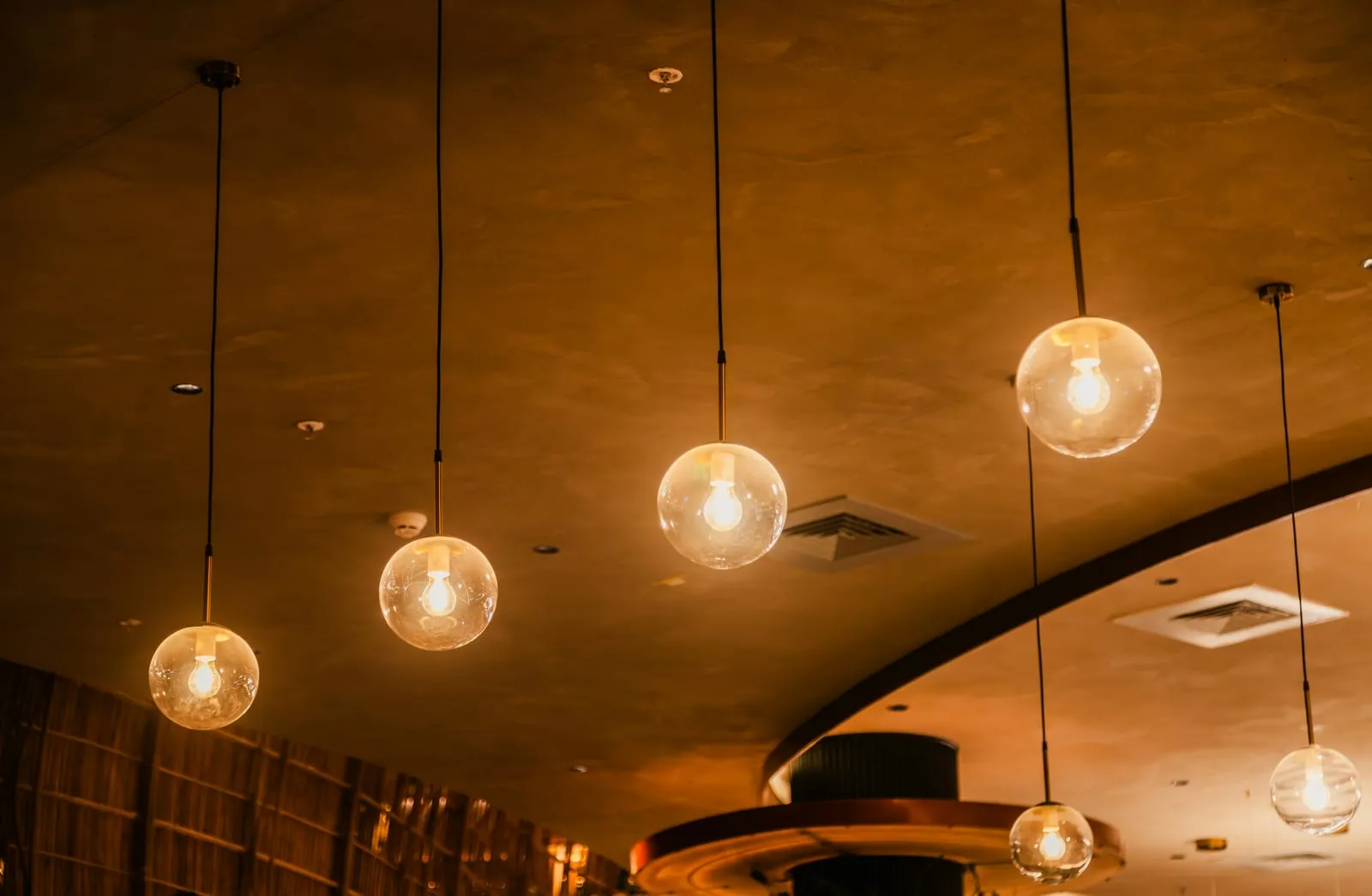 Row of matching glass globe pendant lights with warm LED bulbs across a hospitality ceiling