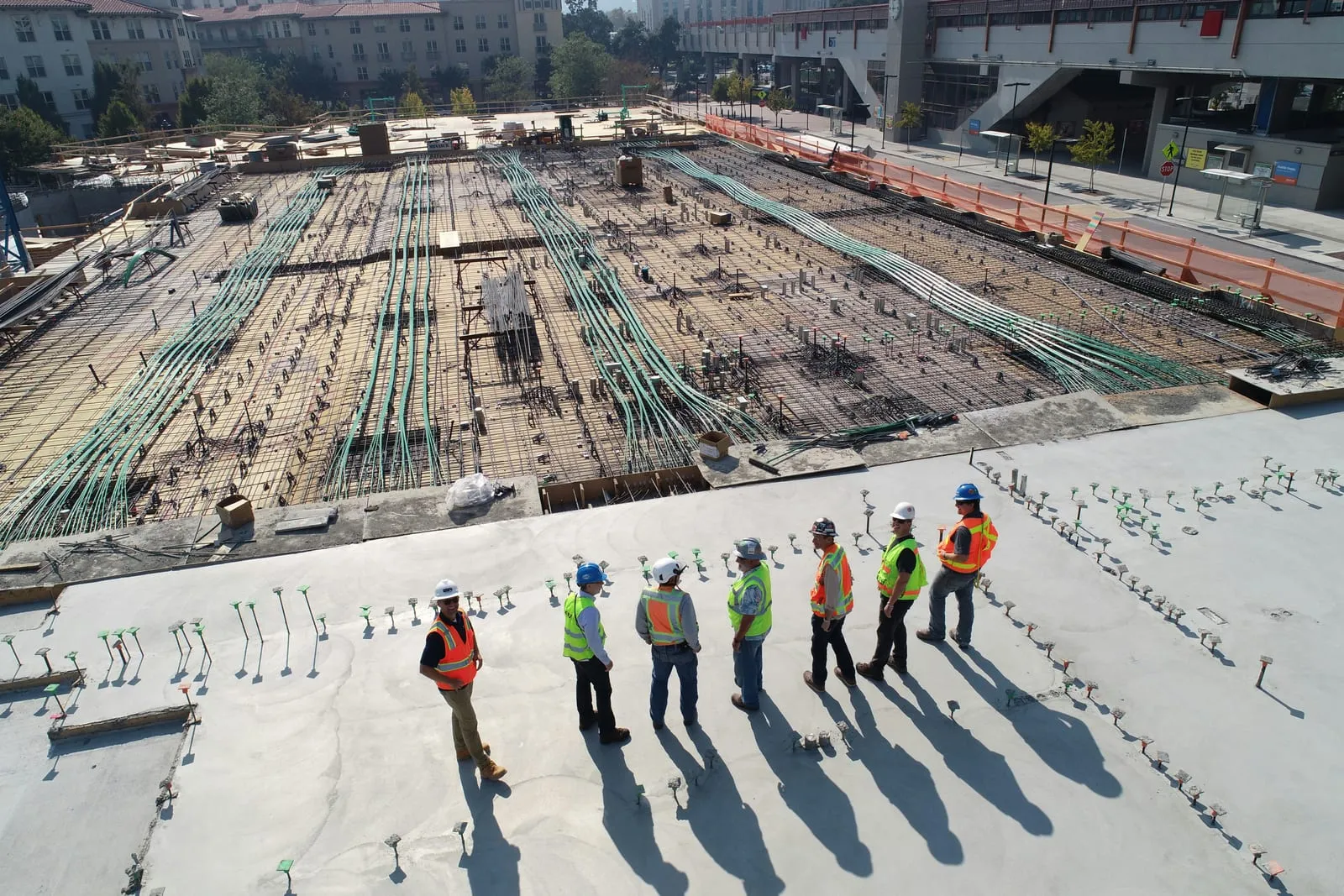 Construction crew in hard hats and safety vests on a multifamily project deck during the structural phase