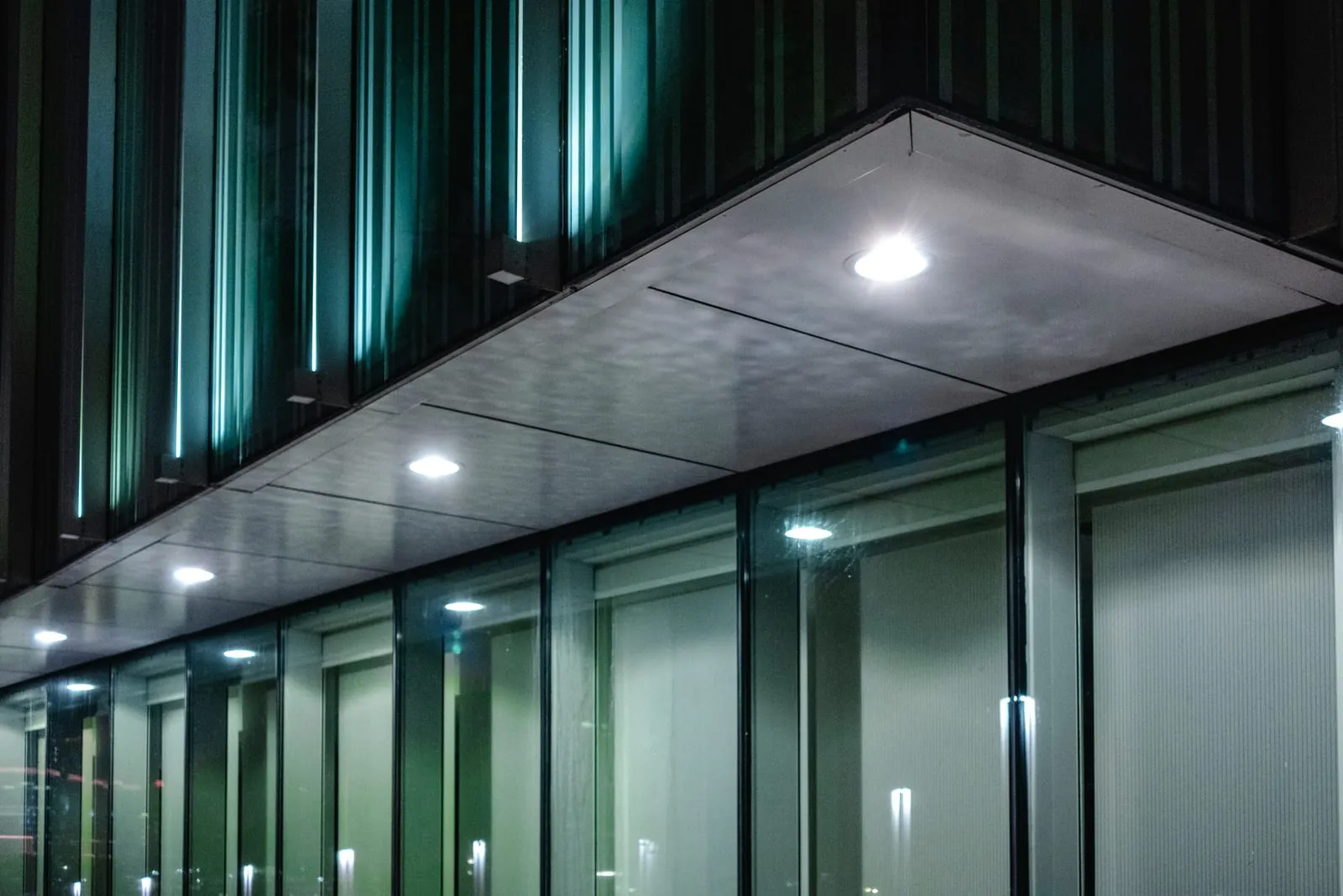 Commercial building facade at night lit by spec-grade LED soffit downlights and an illuminated glass curtain wall